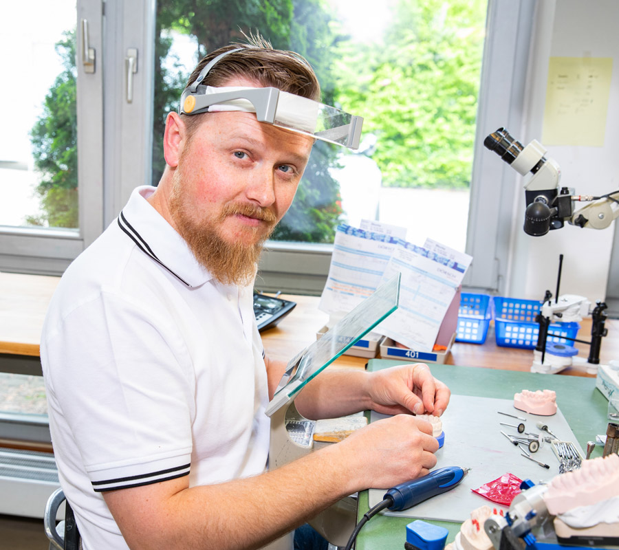 Zahntechniker bei der Arbeit an einem Zahnersatzmodell in einem modernen Dentallabor, umgeben von Werkzeugen und technischen Geräten.